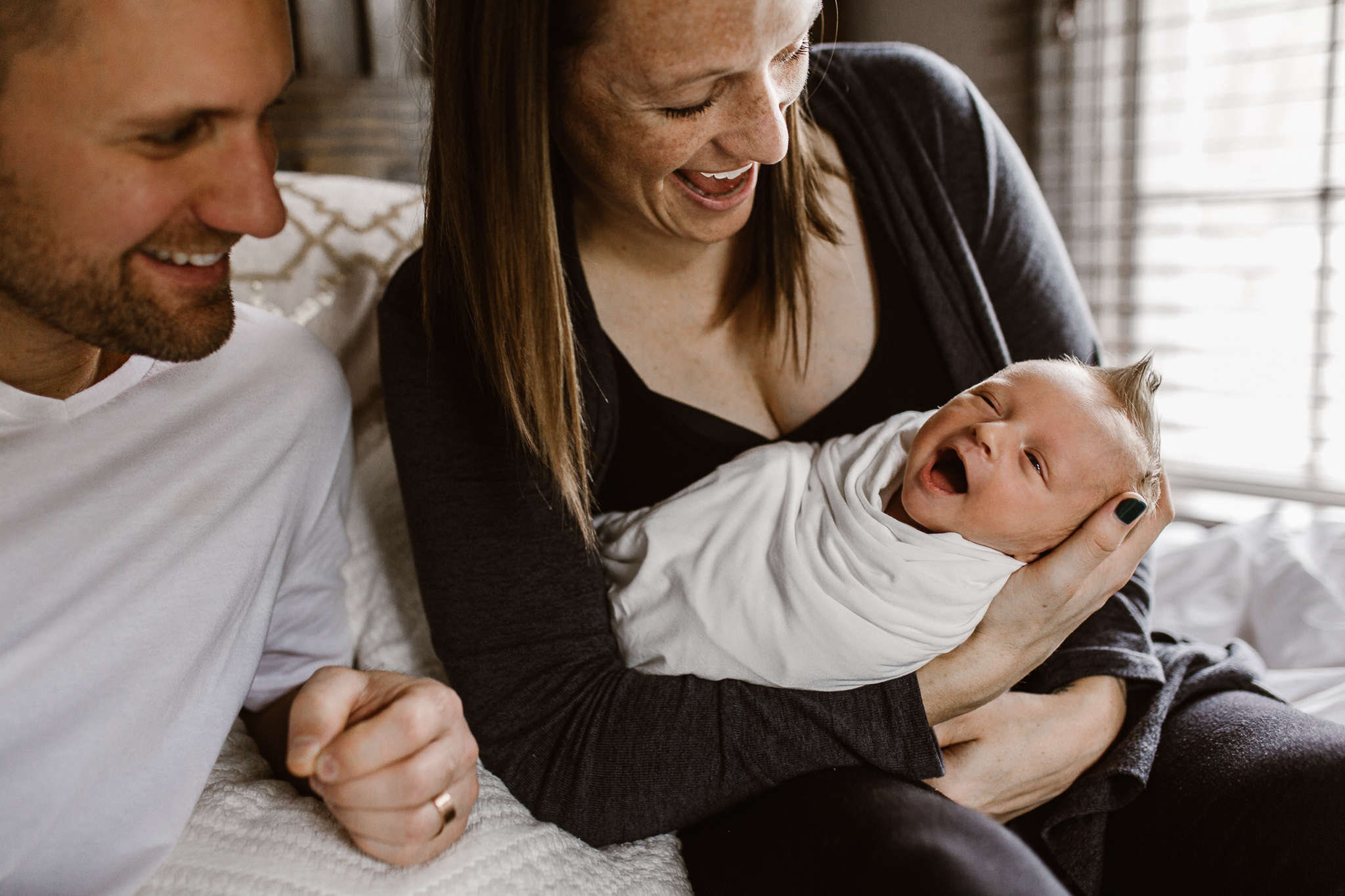New parents smiling down at their baby's expressive smile.